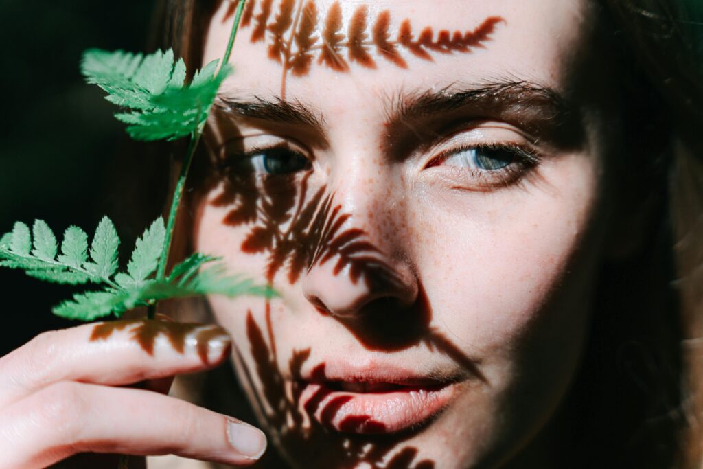 A close-up artistic portrait with fern leaf shadows casting on a woman's face.
